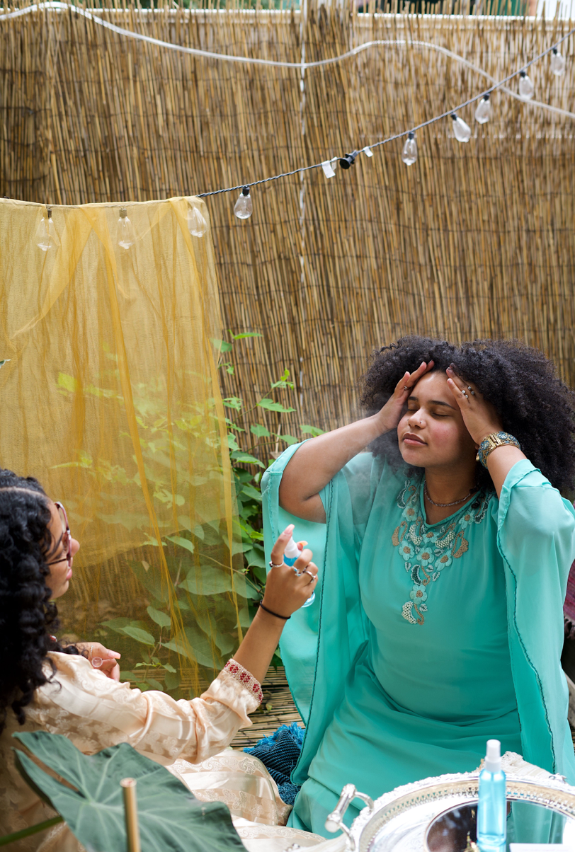 One model sprays the Rose Water while the other soaks it in and lathers it on to her skin